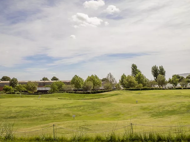 Campo de golf con green y banderas bajo cielo parcialmente nublado