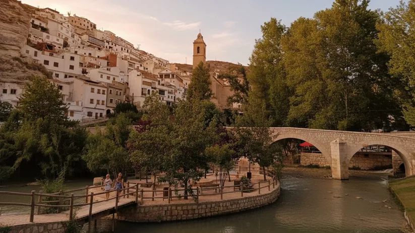 Paseo junto al río con puente de piedra y casas blancas