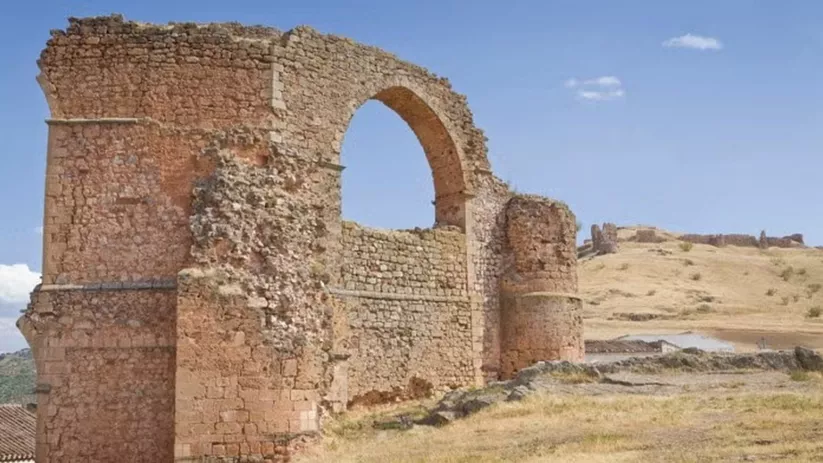 Restos de acueducto de piedra con gran arco sobre una colina de terreno seco y hierba.