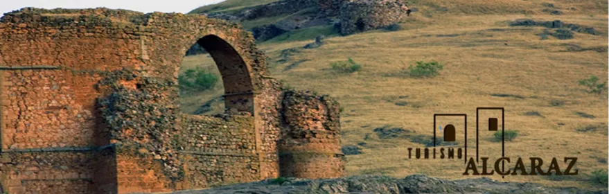 Restos de construcción de piedra con arco central sobre una ladera cubierta de pasto.
