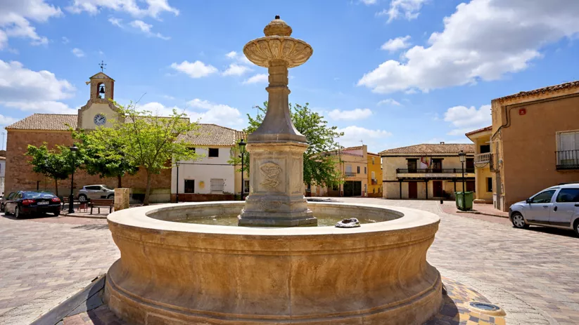 Fuente de piedra en plaza soleada con iglesia y casas
