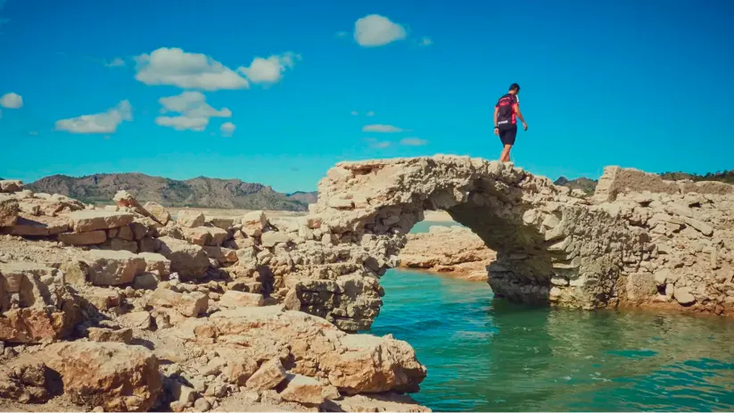 Vista de una persona paseando sobre un puente de piedras sobre agua