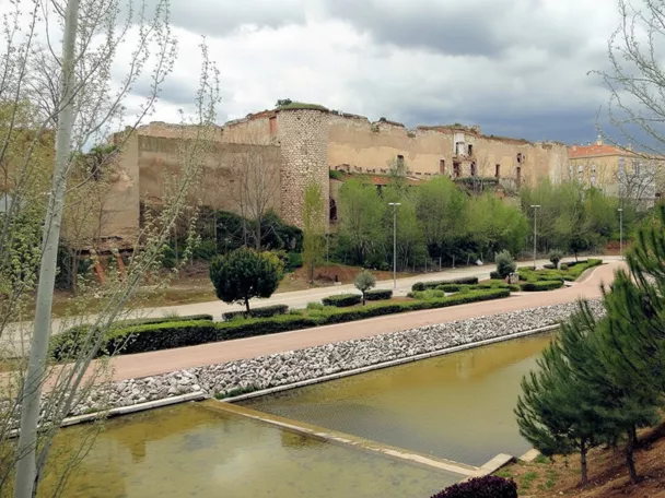 Murallas en ruinas junto a parque y estanque.