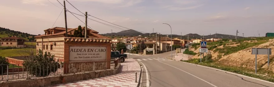Entrada a la localidad con carretera, acera y viviendas al fondo