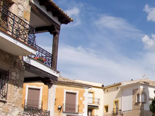 Calle tradicional con balcones de forja y torre de piedra con reloj.