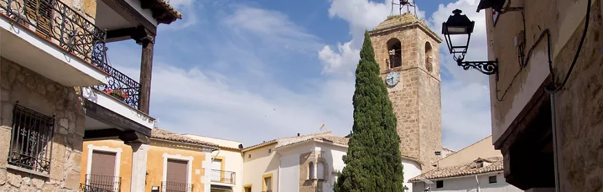 Calle tradicional con balcones de forja y torre de piedra con reloj.