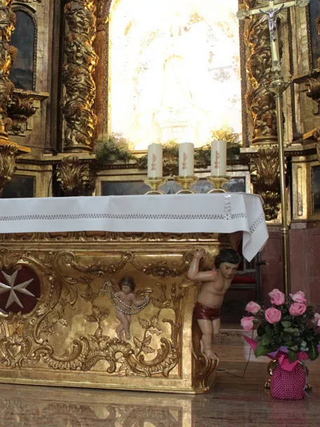Altar dorado con decoración barroca y velas encendidas en el interior de un templo.