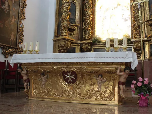 Altar dorado con decoración barroca y velas encendidas en el interior de un templo.