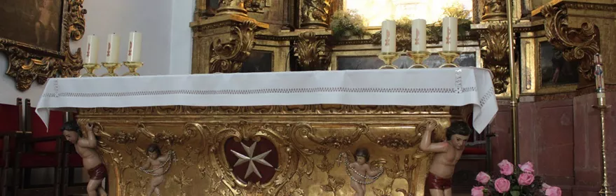 Altar dorado con decoración barroca y velas encendidas en el interior de un templo.