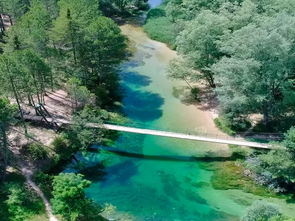 Vista aérea de río de aguas turquesas entre bosque y pasarela