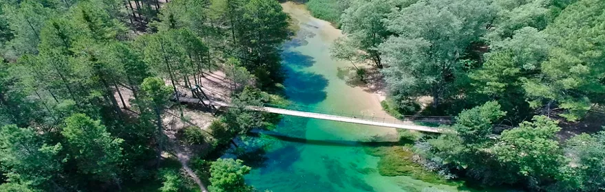 Vista aérea de río de aguas turquesas entre bosque y pasarela