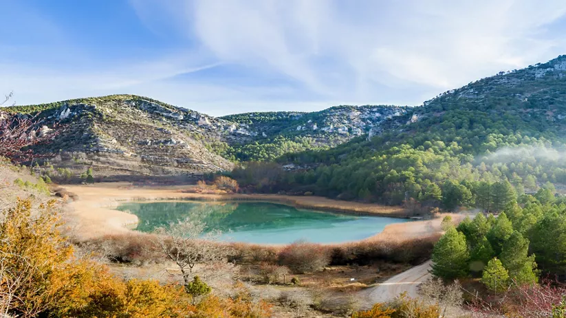 Laguna rodeada de montañas y pinar en paisaje natural