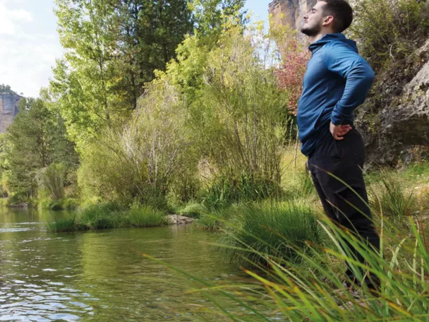 Persona junto a un río de aguas claras rodeado de vegetación y rocas.