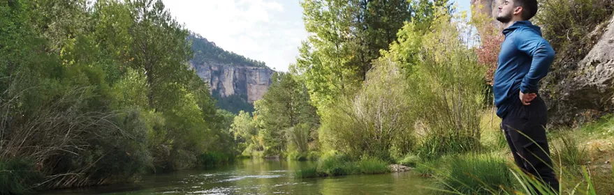 Persona junto a un río de aguas claras rodeado de vegetación y rocas.