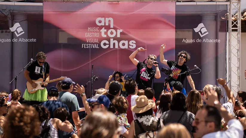 Grupo musical actuando en un escenario al aire libre ante un público numeroso durante el día.