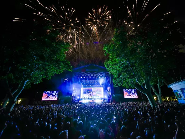 Escenario nocturno con fuegos artificiales sobre el público y pantallas encendidas.