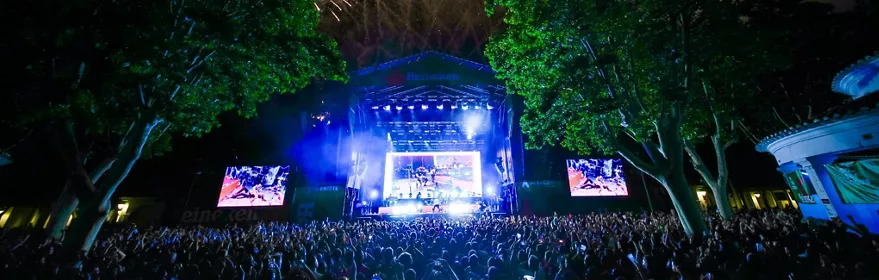 Escenario nocturno con fuegos artificiales sobre el público y pantallas encendidas.