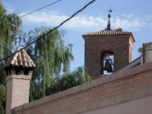 Campanario de ladrillo visto tras un muro y vegetación