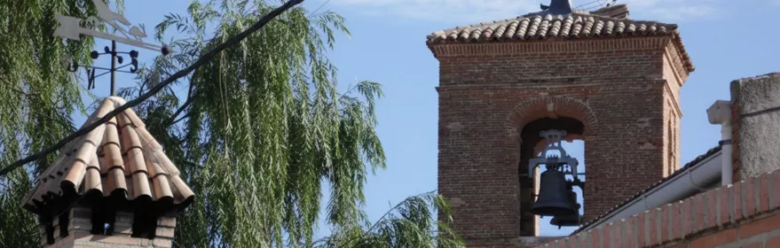 Campanario de ladrillo visto tras un muro y vegetación