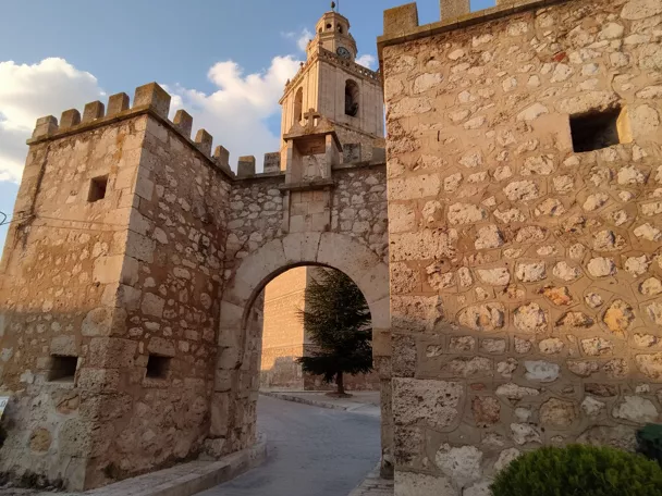 Puerta fortificada con torre y campanario al fondo