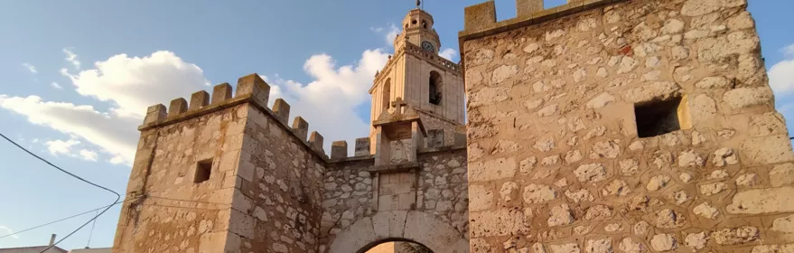 Puerta fortificada con torre y campanario al fondo