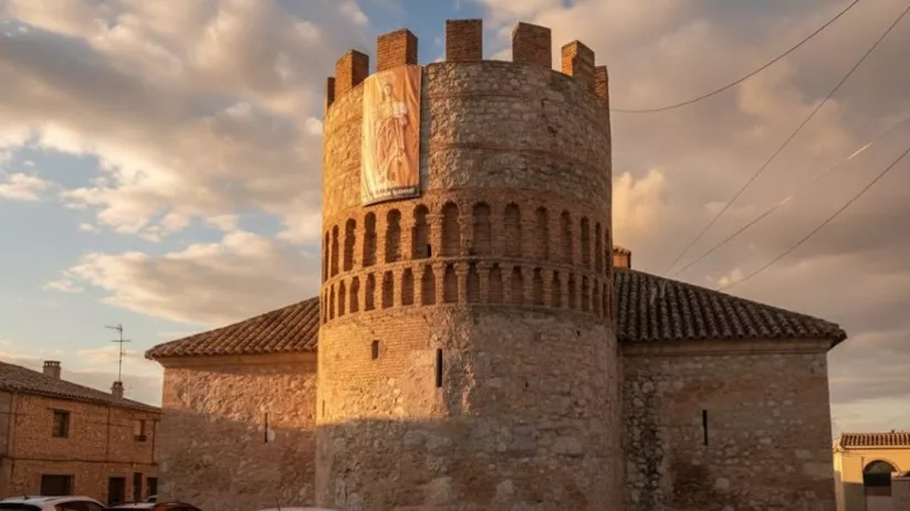 Torre defensiva circular de Arenas de San Juan junto a viviendas del municipio y vehículos estacionados en la plaza.