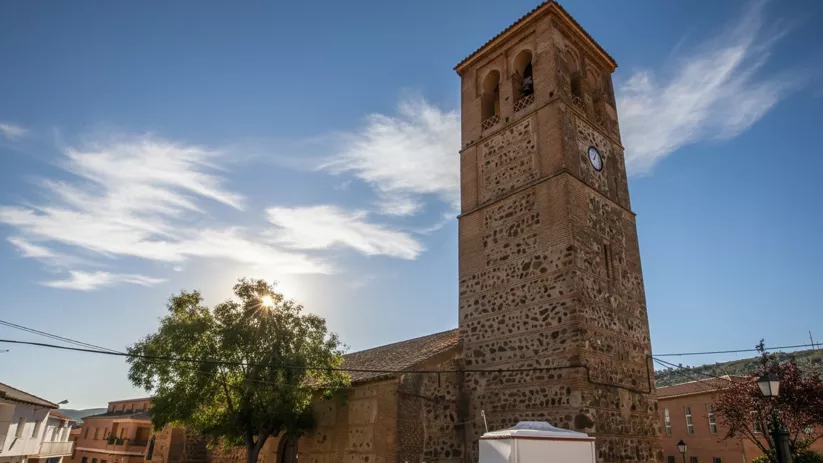 Torre campanario de la iglesia de Arroba de los Montes con reloj visible y plaza en primer plano.