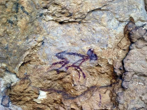 Pintura rupestre de figura animal en roca ocre.