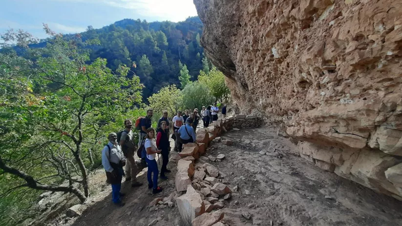 Grupo de personas caminando por un sendero excavado junto a una pared rocosa.