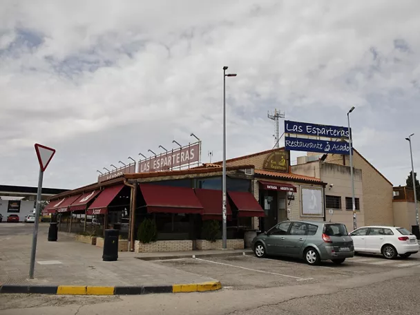 Fachada de restaurante de carretera con terraza y coches aparcados.