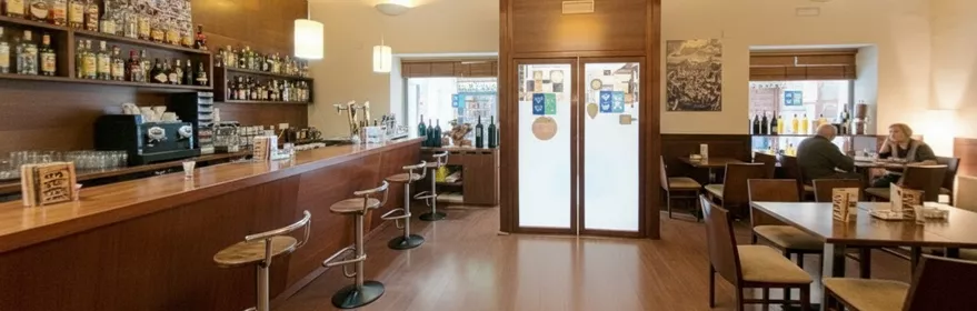 Bar de madera con taburetes y mesas al fondo