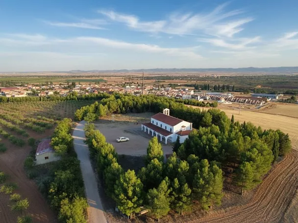 Vista aérea de una ermita rodeada de árboles y campos agrícolas.