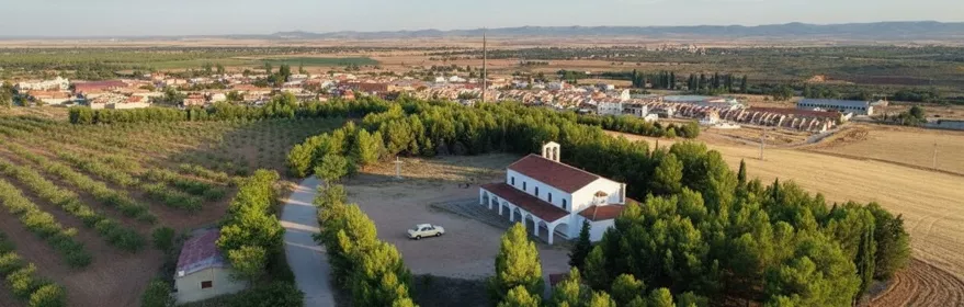 Vista aérea de una ermita rodeada de árboles y campos agrícolas.