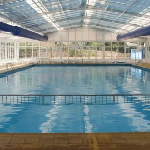 Piscina cubierta con techo acristalado y tumbonas alineadas junto al agua.