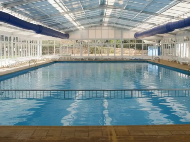Piscina cubierta con techo acristalado y tumbonas alineadas junto al agua.