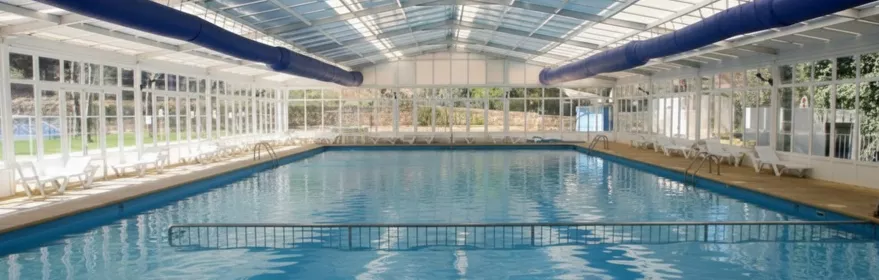 Piscina cubierta con techo acristalado y tumbonas alineadas junto al agua.