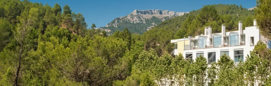Fachada de hotel entre pinos, con sierra rocosa al fondo y cielo azul.