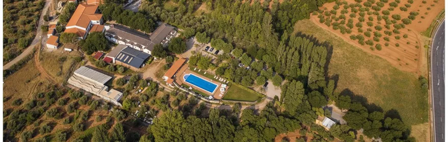Vista aérea de complejo rural con piscina rectangular, edificios y campos de cultivo alrededor.