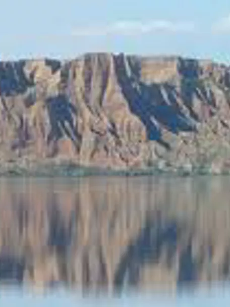 Reflejo de acantilados y colinas en aguas calmadas del embalse.