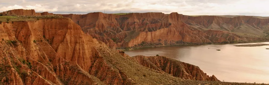Acantilados de tierra rojiza junto a un embalse