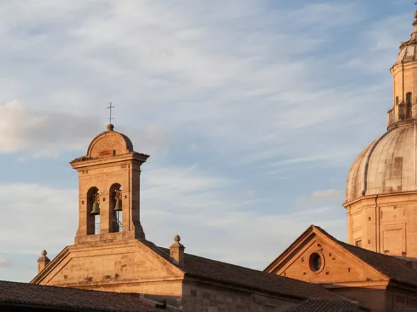 Panorámica de tejados y campanario con cúpula al atardecer, bajo cielo con nubes.