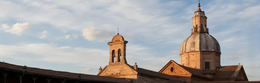 Panorámica de tejados y campanario con cúpula al atardecer, bajo cielo con nubes.