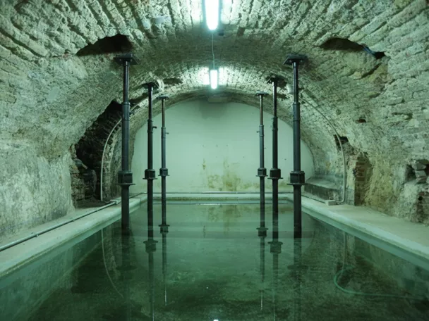 Sala abovedada con estanque de agua y pilares metálicos en el interior.