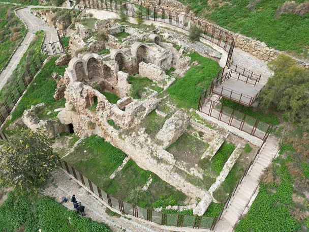 Conjunto arqueológico amurallado con arcos reconstruidos y senderos perimetrales.