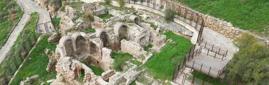 Conjunto arqueológico amurallado con arcos reconstruidos y senderos perimetrales.