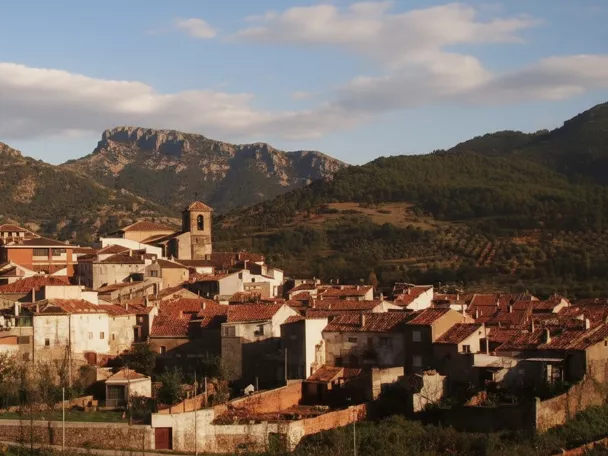 Panorámica de pueblo con tejados rojizos e iglesia frente a la sierra