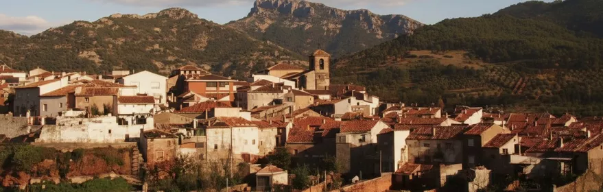 Panorámica de pueblo con tejados rojizos e iglesia frente a la sierra
