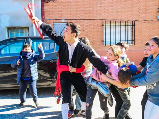Jóvenes con trajes tradicionales y palos rojos en la calle.