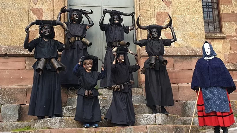 Grupo con máscaras negras y cuernos frente a iglesia.
