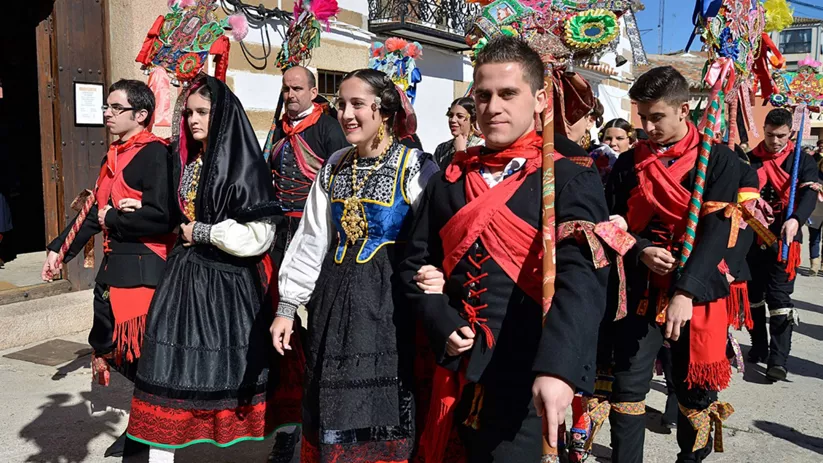 Desfile de personas con trajes tradicionales y varas decoradas por la calle.
